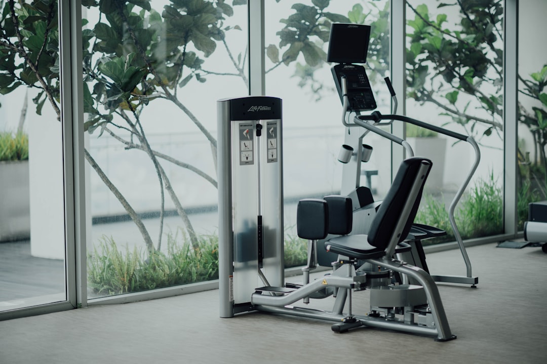 Life Fitness strength training equipment in a bright, modern gym with floor-to-ceiling windows overlooking lush green plants outdoors.